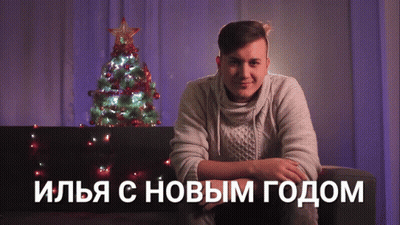 A Man Sits On A Couch In Front Of A Christmas Tree With Russian Writing On The Bottom GIF