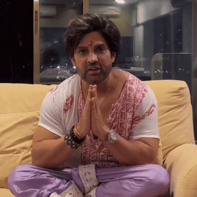 A Man Sits On A Couch With His Hands Folded In Front Of His Face GIF