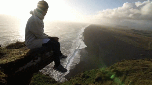 A Man Sits On A Ledge Overlooking The Ocean GIF
