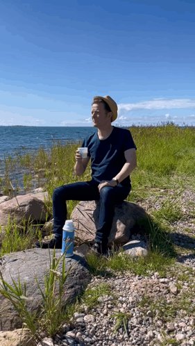 A Man Sits On A Rock Drinking From A Thermos GIF