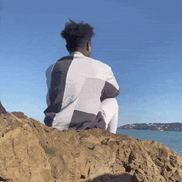 A Man Sits On A Rock Looking Out Over The Ocean GIF