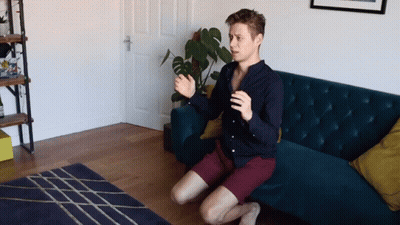 A Man Sits On His Knees In Front Of A Couch GIF