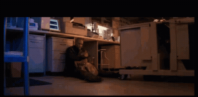 A Man Sits On The Floor In Front Of A Desk With A Computer Monitor On It GIF