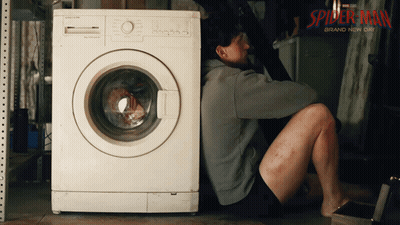 A Man Sits On The Floor Next To A Washing Machine That Says Spider-Man Brand Now On It GIF