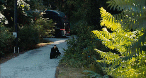 A Man Sits On The Side Of A Road In Front Of A Truck GIF