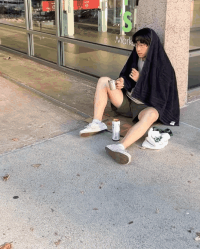 A Man Sits On The Sidewalk In Front Of A Store That Says Mark 'S GIF