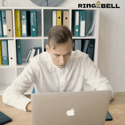 A Man Sitting At A Desk Looking At A Laptop With Ring The Bell Written On The Bottom GIF