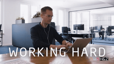 A Man Sitting At A Desk With A Laptop And The Words Working Hard On The Bottom GIF
