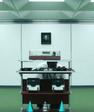 A Man Sitting At A Desk With A Picture Of A Man On The Wall Above Him GIF