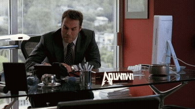 A Man Sitting At A Desk With A Sign That Says Aquafina GIF