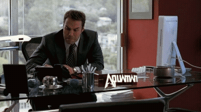 A Man Sitting At A Desk With A Sign That Says Aquafina GIF
