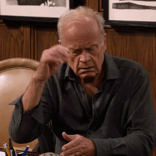 A Man Sitting At A Desk With His Hands Folded In Front Of Him GIF