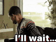 A Man Sitting At A Desk With The Words I 'Ll Wait GIF