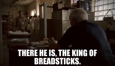 A Man Sitting At A Desk With The Words " There He Is The King Of Breadsticks " GIF