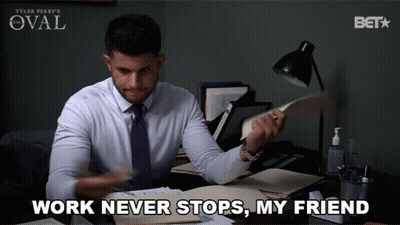 A Man Sitting At A Desk With The Words " Work Never Stops My Friend " Written Below Him GIF