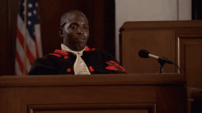A Man Sitting At A Podium In Front Of A Microphone With An American Flag In The Background GIF