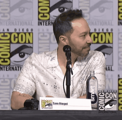 A Man Sitting At A Table At Comic Con GIF