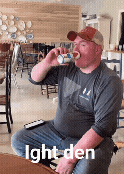 A Man Sitting At A Table Drinking From A Cup With The Words Ight Den Below Him GIF