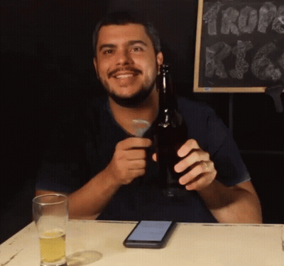 A Man Sitting At A Table Holding A Beer Bottle GIF