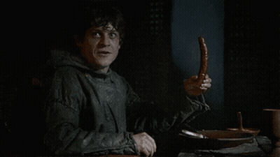 A Man Sitting At A Table Holding A Sausage In His Hand . GIF