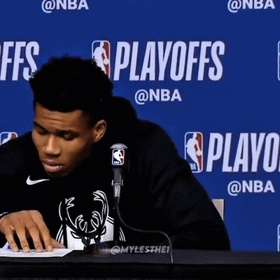 A Man Sitting At A Table In Front Of A Blue Wall That Says Playoffs On It GIF