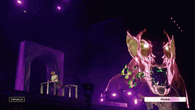 A Man Sitting At A Table In Front Of A Stage With A Sign That Says " Flume " On It GIF