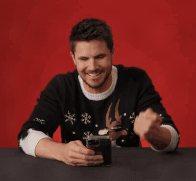 A Man Sitting At A Table Looking At A Cell Phone With The Words That 'S Funny On The Bottom GIF
