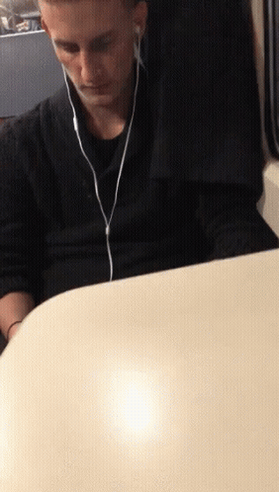 A Man Sitting At A Table Wearing Ear Buds GIF
