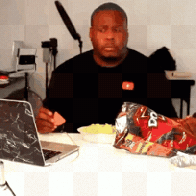 A Man Sitting At A Table With A Bag Of Doritos And A Laptop GIF