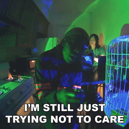 A Man Sitting At A Table With A Cage In The Background And The Words I 'M Still Just Trying GIF