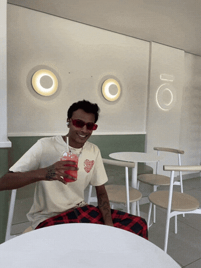 A Man Sitting At A Table With A Drink In His Hand GIF