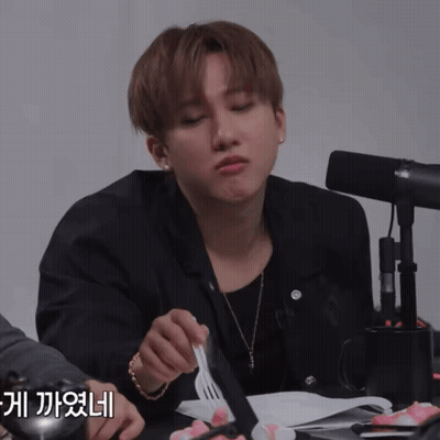 A Man Sitting At A Table With A Fork In His Hand And A Microphone In The Background GIF