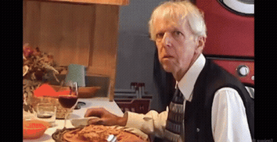 A Man Sitting At A Table With A Glass Of Wine And A Plate Of Pizza GIF