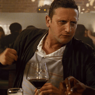 A Man Sitting At A Table With A Glass Of Wine In Front Of Him GIF