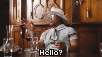 A Man Sitting At A Table With A Hat And Glasses Says Hello GIF