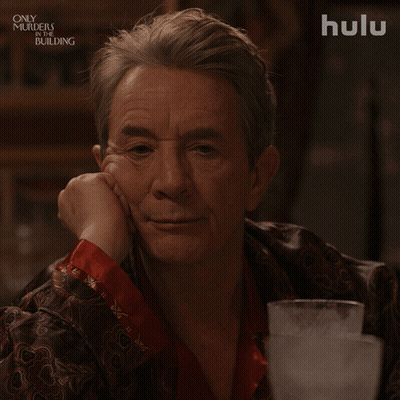 A Man Sitting At A Table With A Hulu Logo Behind Him GIF