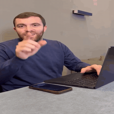 A Man Sitting At A Table With A Laptop And Cell Phone GIF
