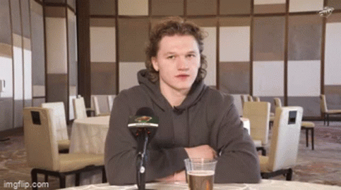 A Man Sitting At A Table With A Microphone And A Glass Of Beer . GIF