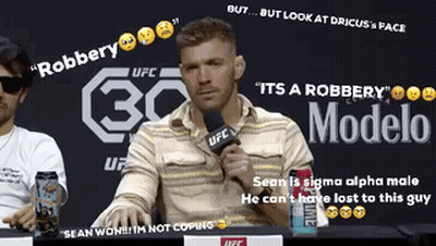 A Man Sitting At A Table With A Microphone In Front Of A Sign That Says Modelo GIF