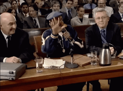 A Man Sitting At A Table With A Microphone In Front Of Him GIF