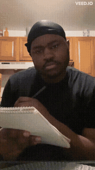A Man Sitting At A Table With A Notebook And A Pen And The Words Veed.io On The Bottom Right GIF