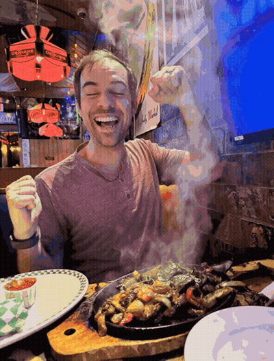 A Man Sitting At A Table With A Plate Of Food And A Sign That Says Georges On It GIF
