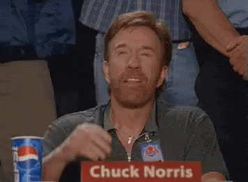 A Man Sitting At A Table With A Sign That Says Chuck Norris On It GIF