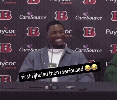 A Man Sitting At A Table With A Sign That Says " First Ijboled Then I Serious " GIF