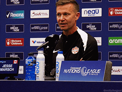 A Man Sitting At A Table With A Sign That Says Nations League Finals GIF