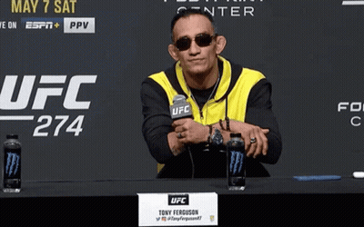 A Man Sitting At A Table With A Sign That Says Ufc GIF