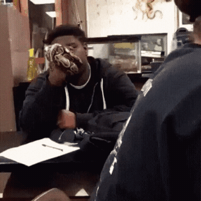 A Man Sitting At A Table With A Snake On His Face GIF