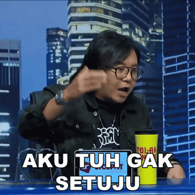 A Man Sitting At A Table With A Yellow Cup That Says Aku Tuh Gak Setuju On It GIF