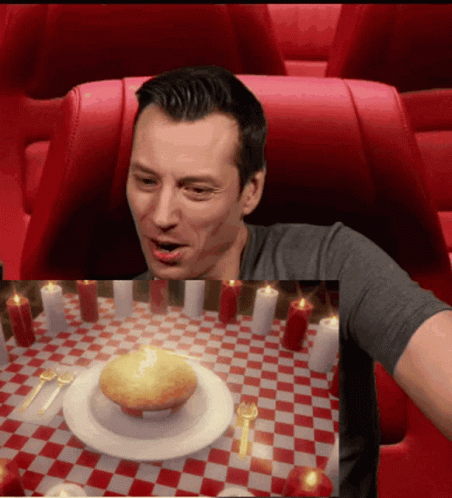 A Man Sitting At A Table With Candles And A Plate Of Food GIF