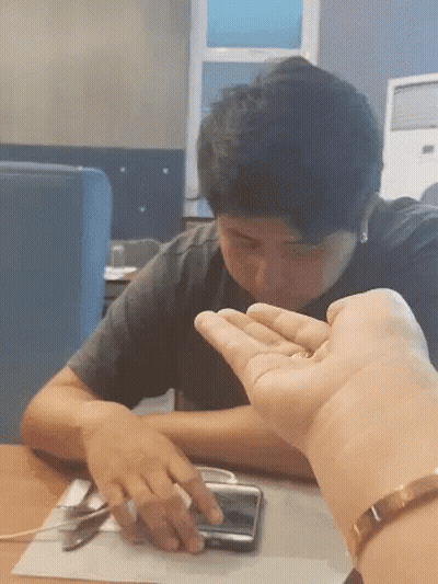 A Man Sitting At A Table With His Hand On A Phone GIF